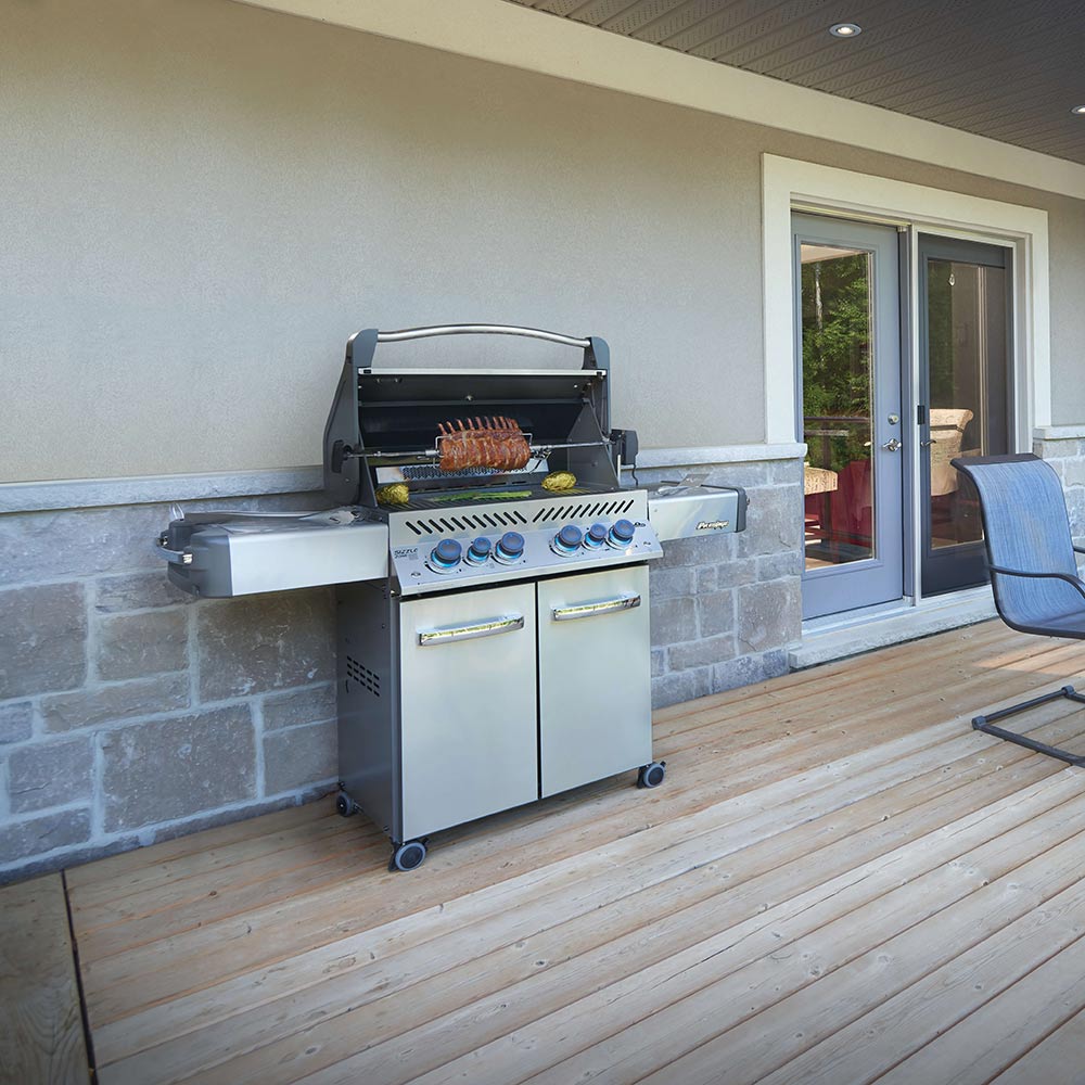 Stainless steel gas grill on cart on an outdoor patio with two cabinet doors