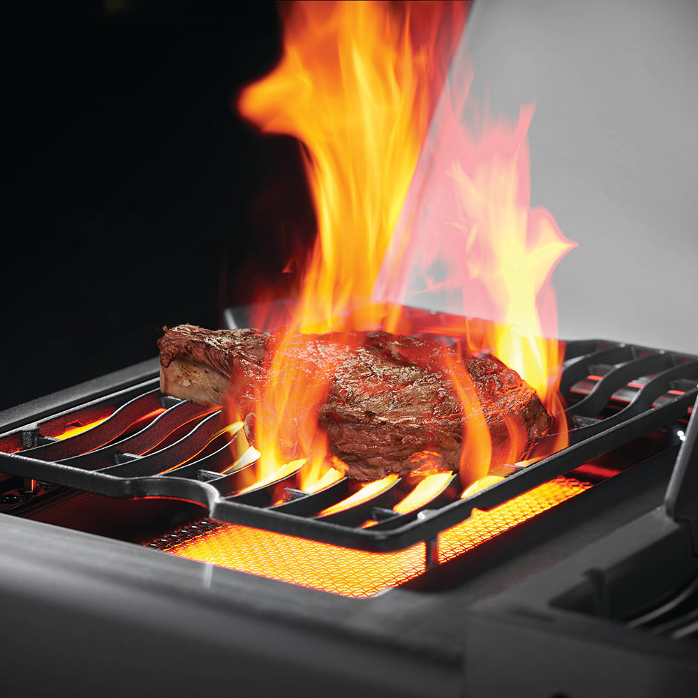 Gas grill firebox with a steak over grates and flames rising