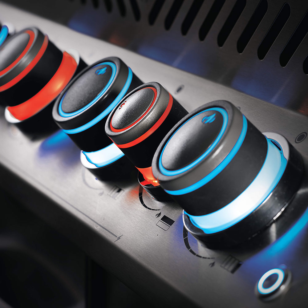 Gas grill control knobs on the front panel with blue-lit ignition rings