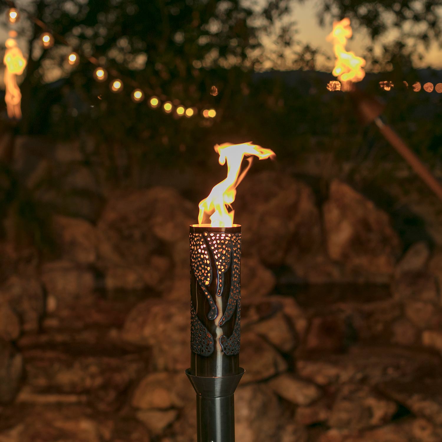Decorative gas torch head with open top, lit flame visible above textured bronze body