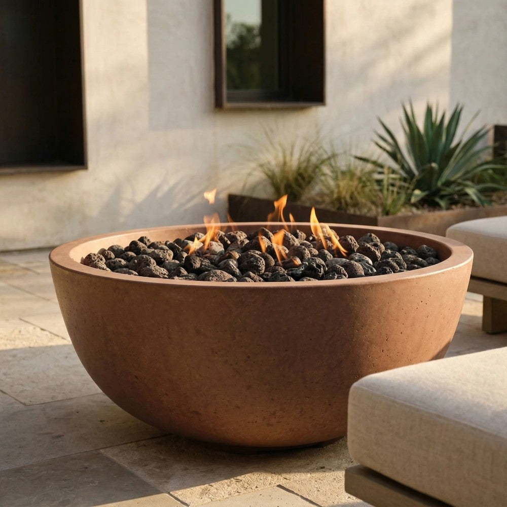 Brown concrete gas fire pit bowl with flames and black lava rocks on patio