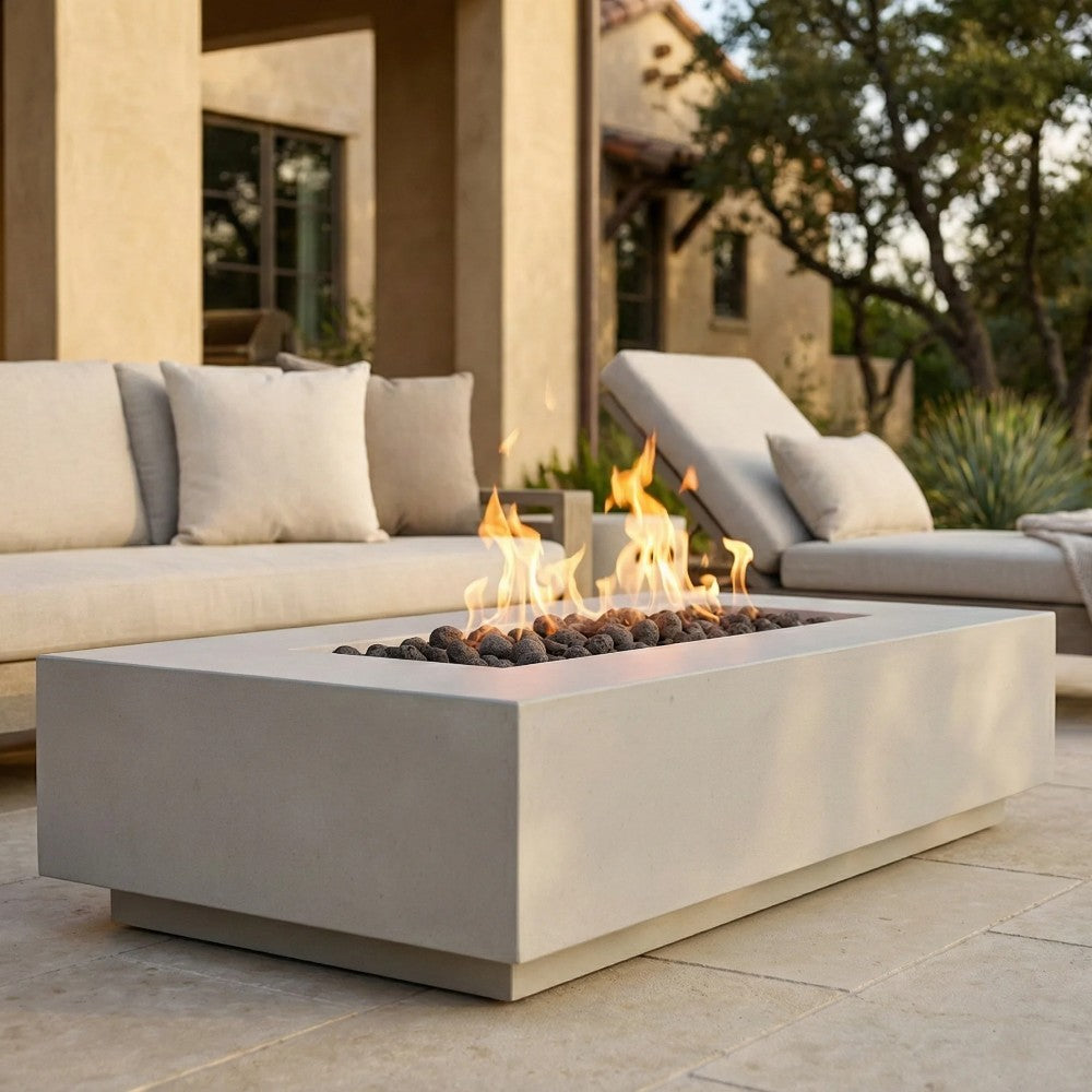 Light-colored rectangular concrete gas fire pit with flame and black lava rocks