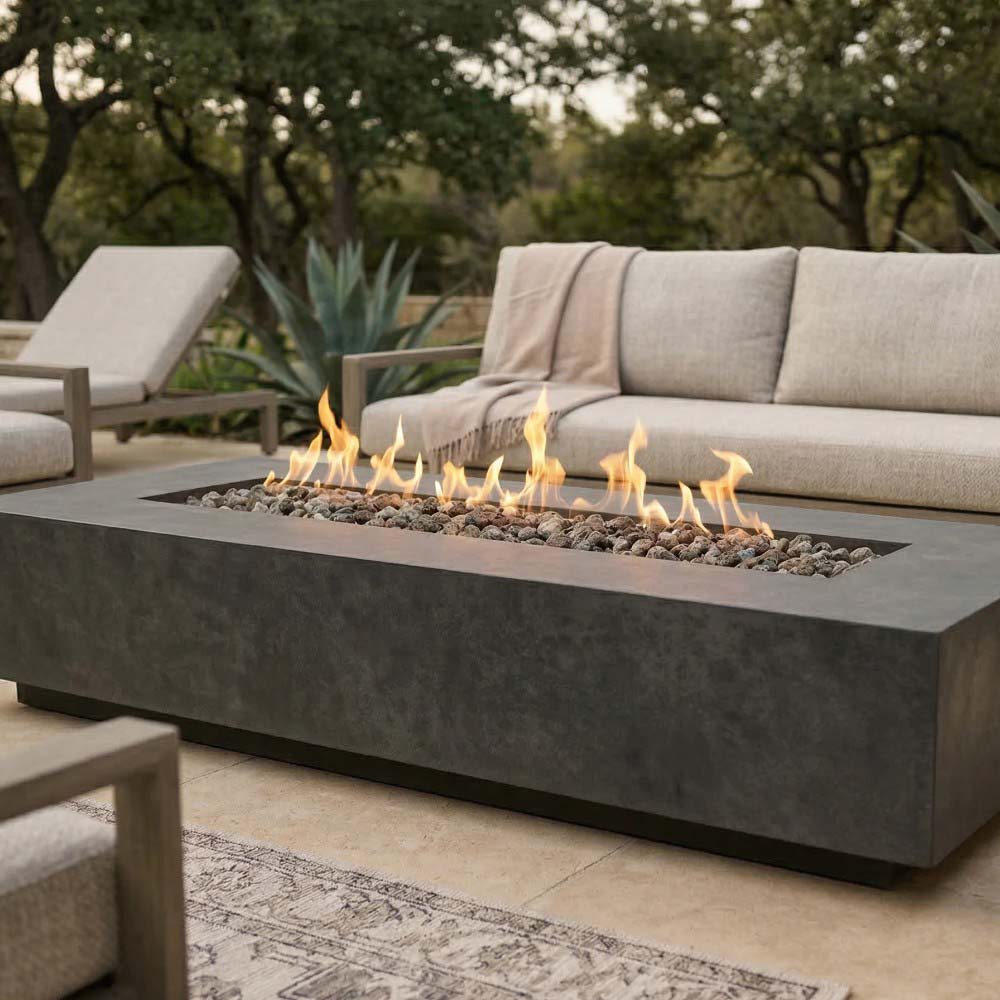 Low rectangular concrete gas fire pit in dark gray with flames and black lava rocks