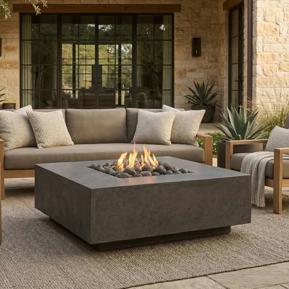 Square concrete gas fire pit with flame and dark lava rocks, set on outdoor patio