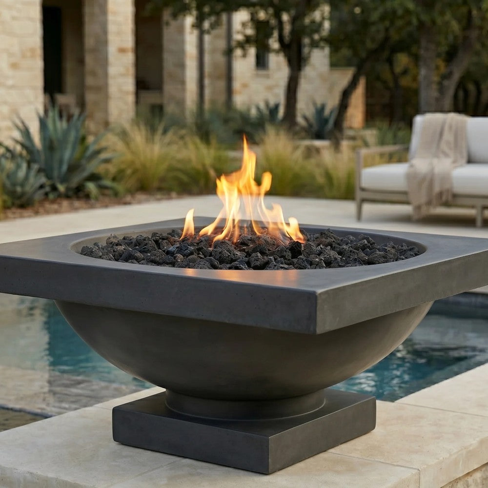 Concrete gas fire bowl with black lava rocks, square rim, and visible open flame