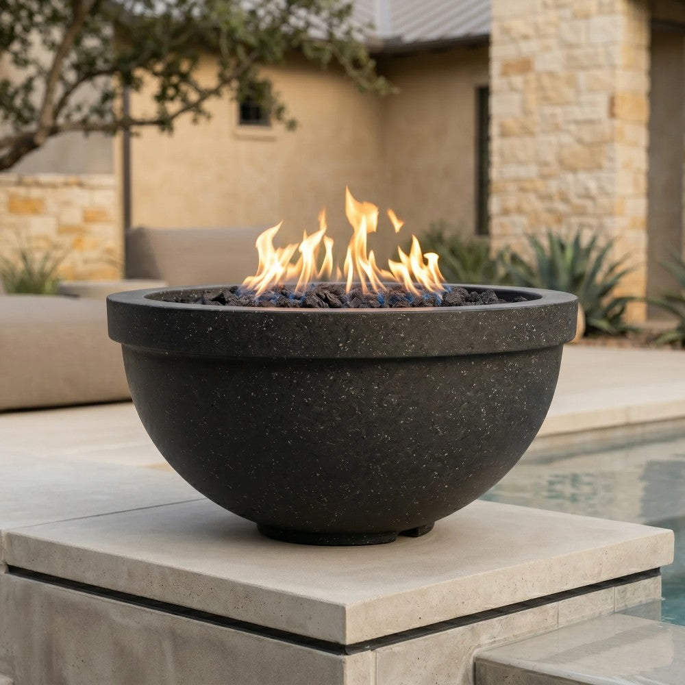 Dark concrete gas fire bowl on stone base with flame burning and lava rock visible.