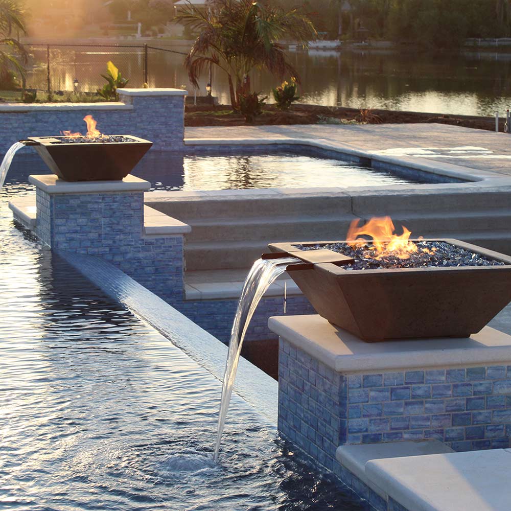 Outdoor concrete gas fire bowl with flames and water spillover into pool edge