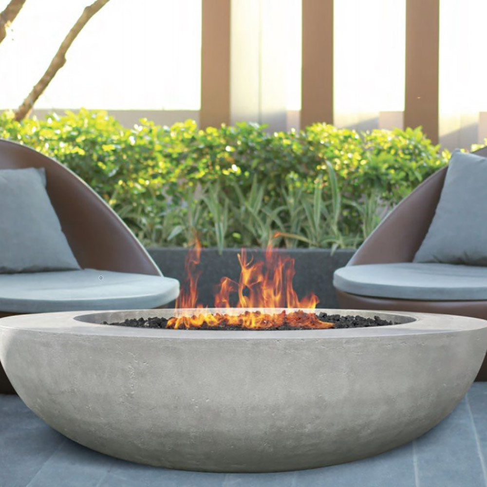 Outdoor concrete gas fire pit bowl with flames above black burner pan and rocks