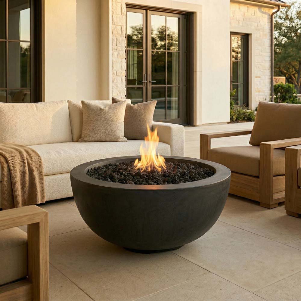 Dark concrete gas fire pit bowl with flame and lava rocks on patio near seating