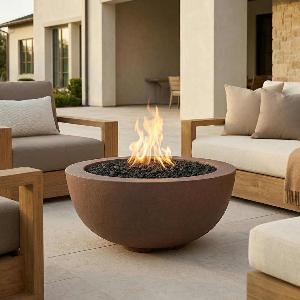 Brown concrete gas fire pit with flame and dark lava rocks between outdoor sofas