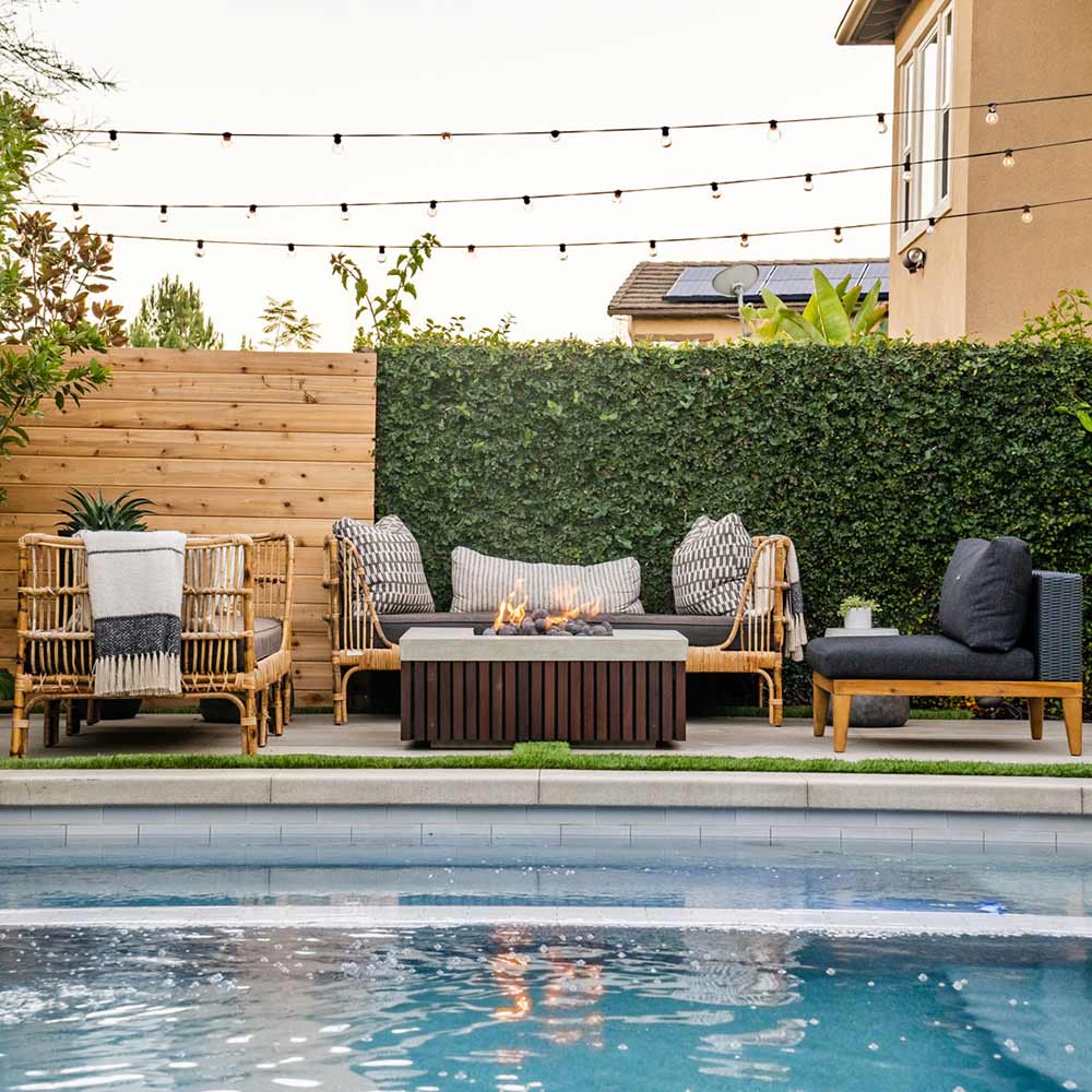 Square gas fire pit with concrete surround and wooden slat panels, with small flames.