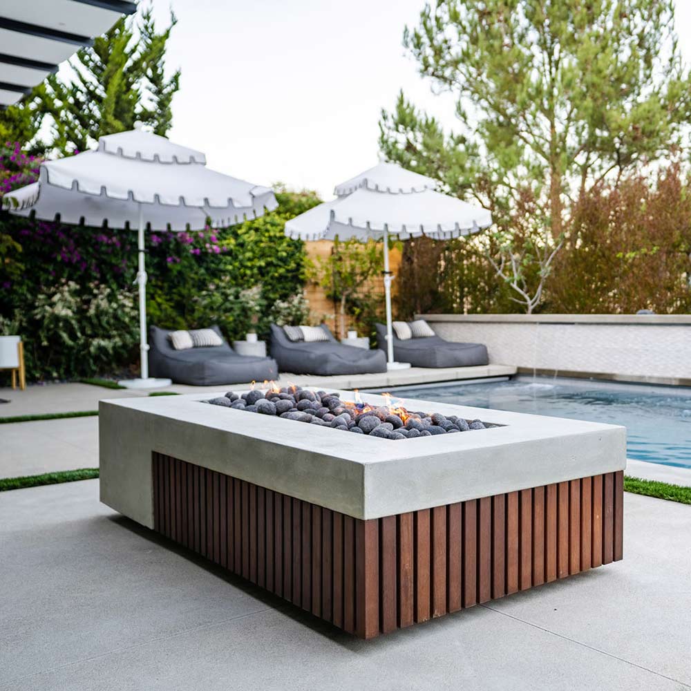 Concrete gas fire pit with dark wood slats and black lava rocks in a rectangular basin