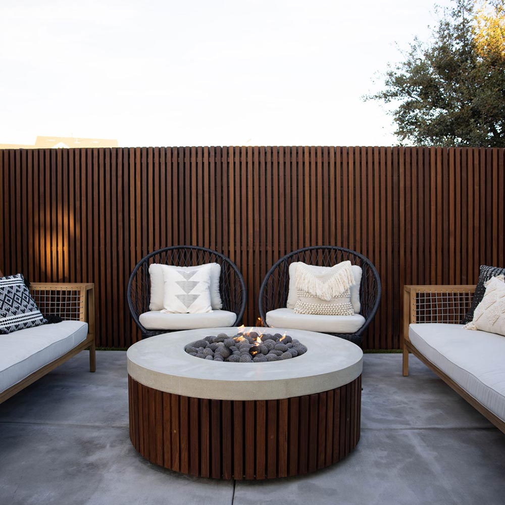 Round concrete gas fire pit with speckled gray top and wood slat base in outdoor seating area