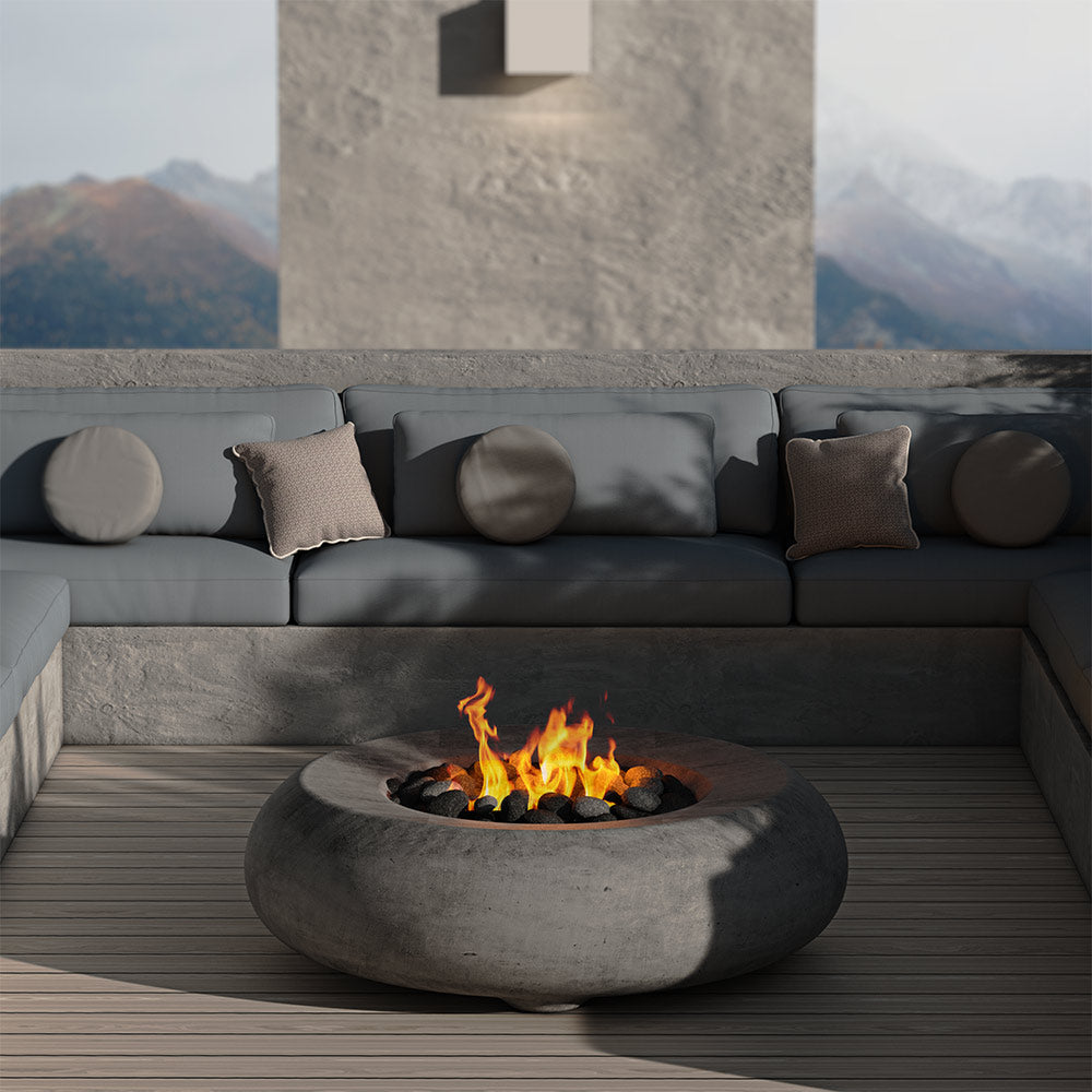 Concrete gas fire bowl with burning flames and dark lava rocks, set on patio decking.