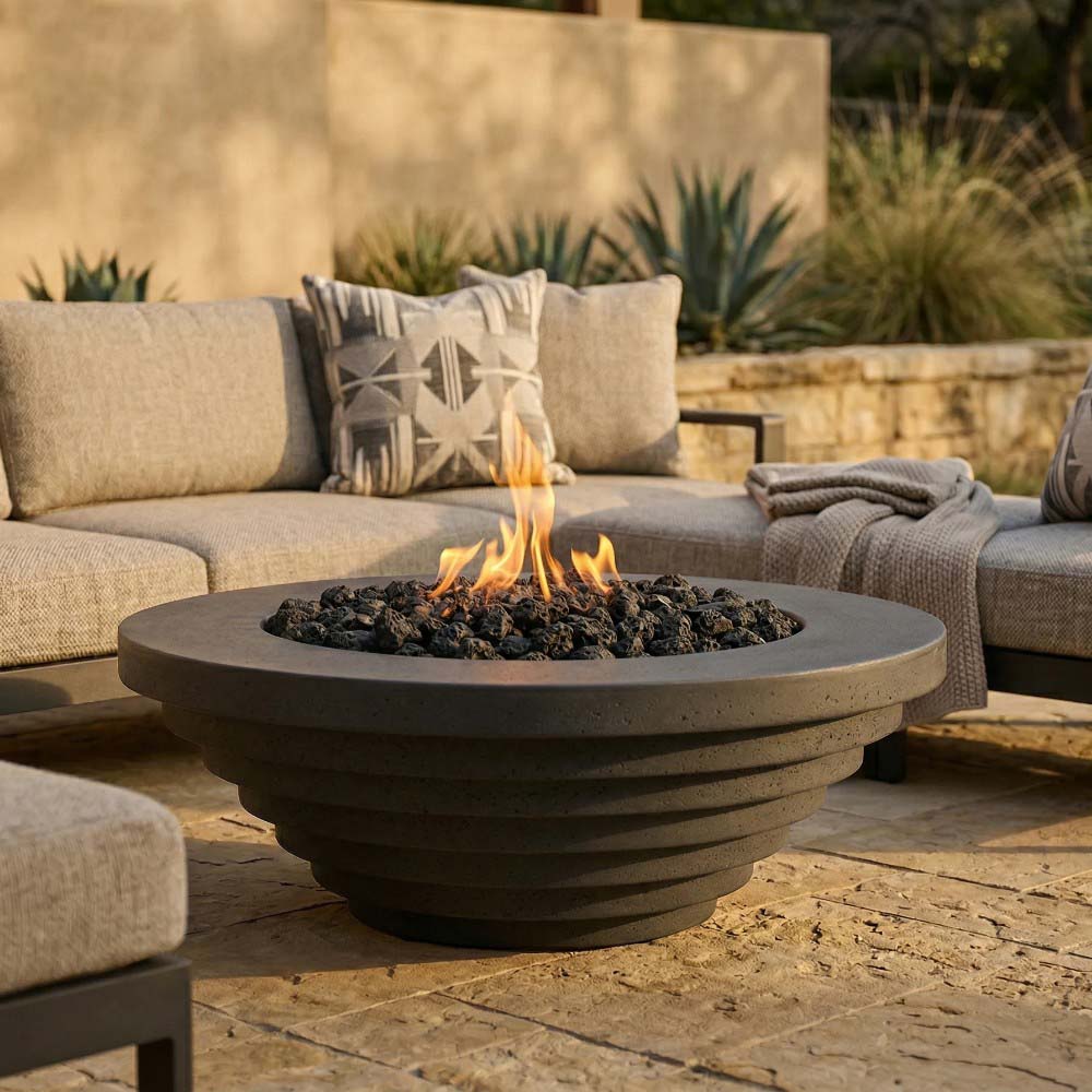 Round concrete gas fire pit with flame over dark lava rocks on outdoor patio