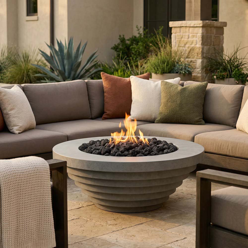 Round concrete gas fire pit with visible flames and dark lava rocks in patio view