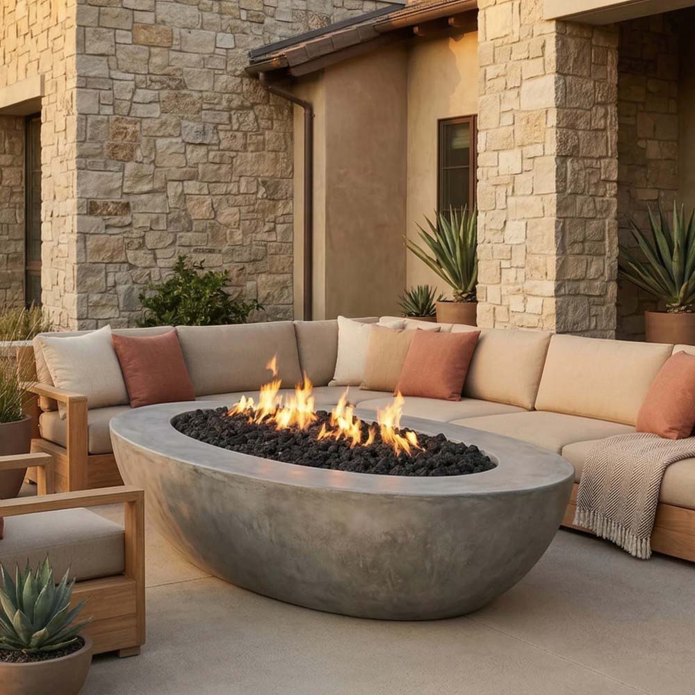Gray oval concrete gas fire pit with flame and black lava rocks