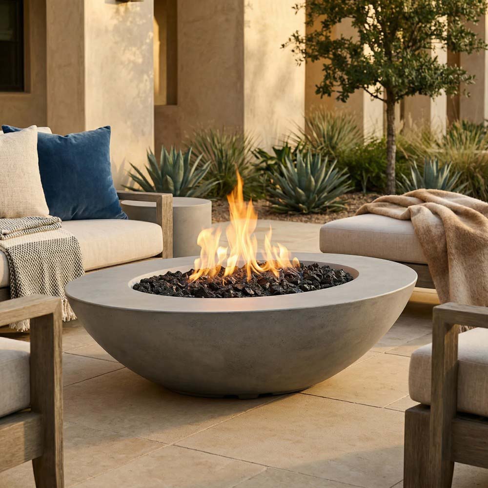 Grey oval concrete gas fire pit with lit flame in center rock bed