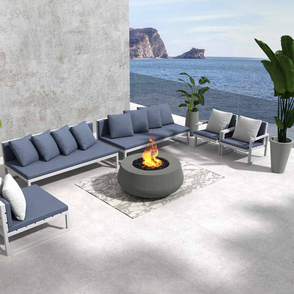 Concrete gas fire bowl with small flames and black burner rocks on patio