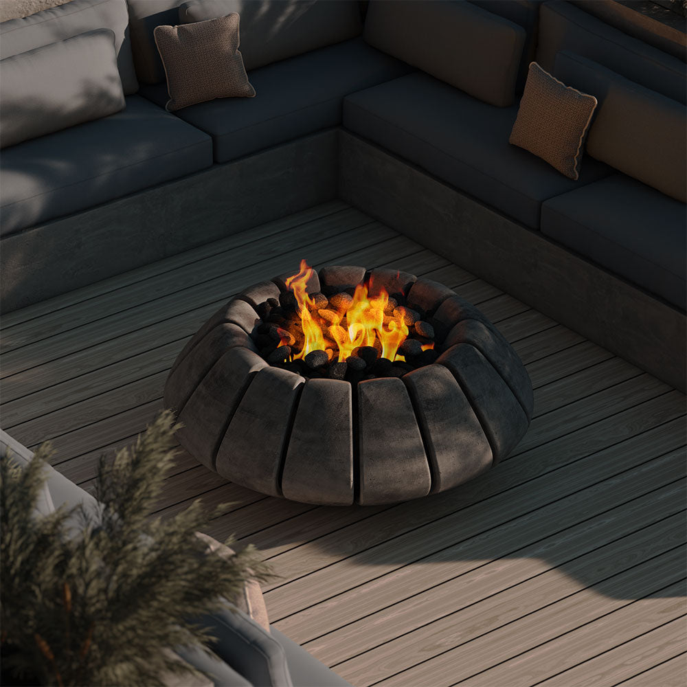 Concrete gas fire bowl with flames and dark lava rocks on an outdoor patio.