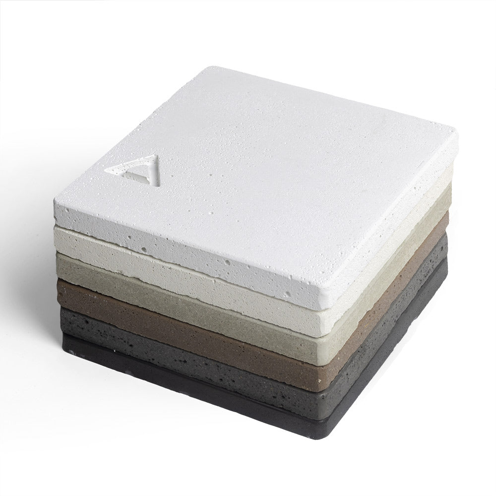 Concrete chip samples stacked, pale white square on top with dark gray base and triangle logo.