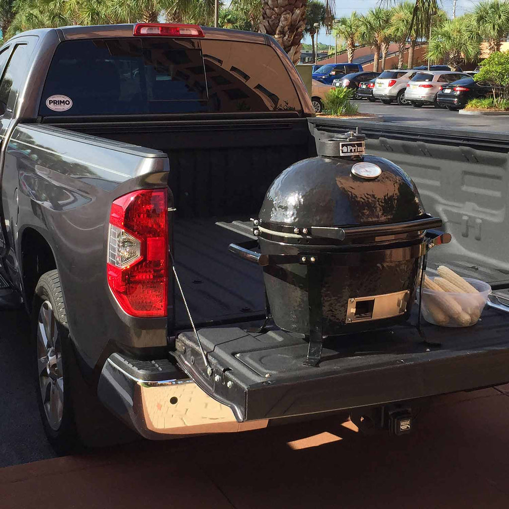 Oval ceramic kamado grill mounted in truck bed on black metal base