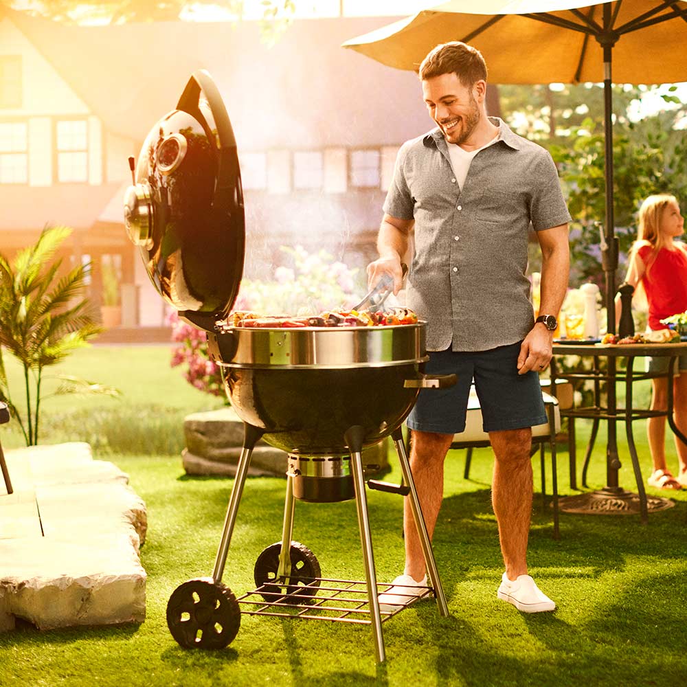 Black charcoal kettle grill open with cooking grate and food inside the bowl