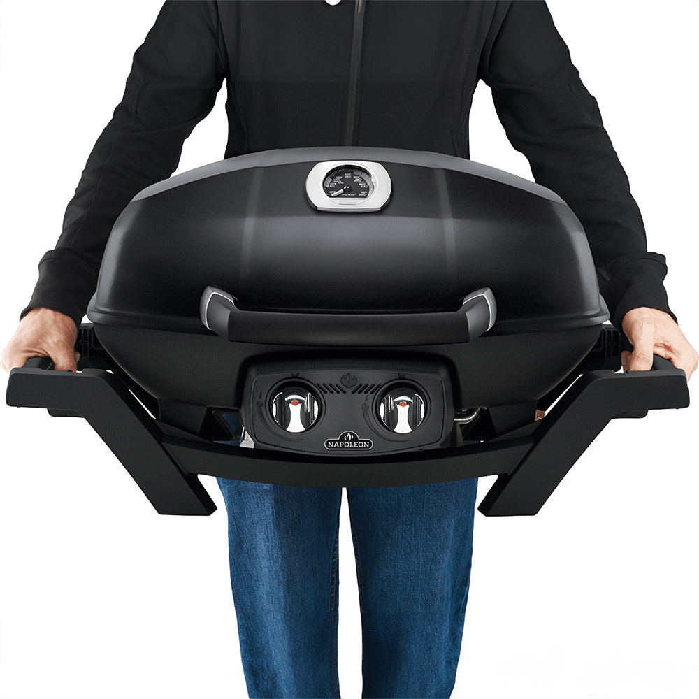 Portable tabletop gas grill on legs with black lid and front knobs, held by person.