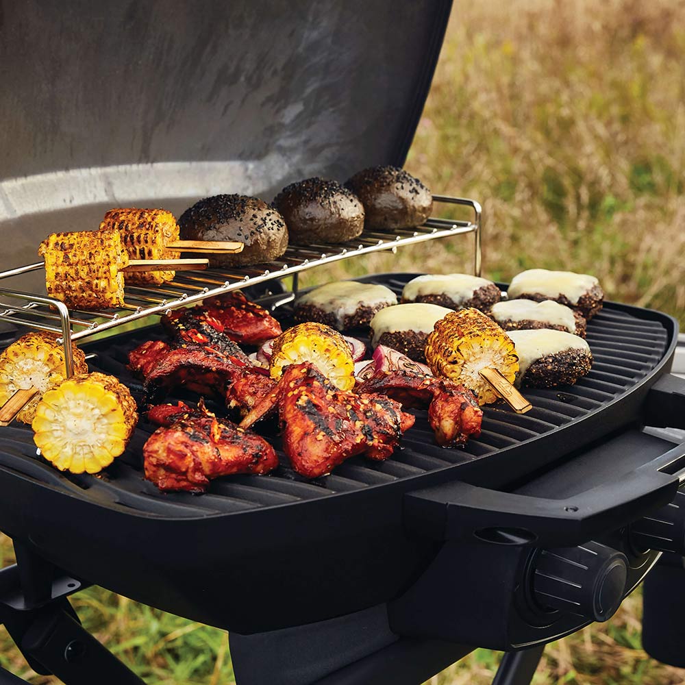 Portable propane grill with grilled meat and vegetables on ridged cooking grate