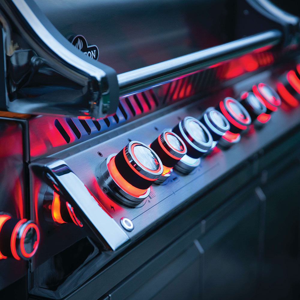 Gas grill burner area with glowing orange flames under the stainless hood