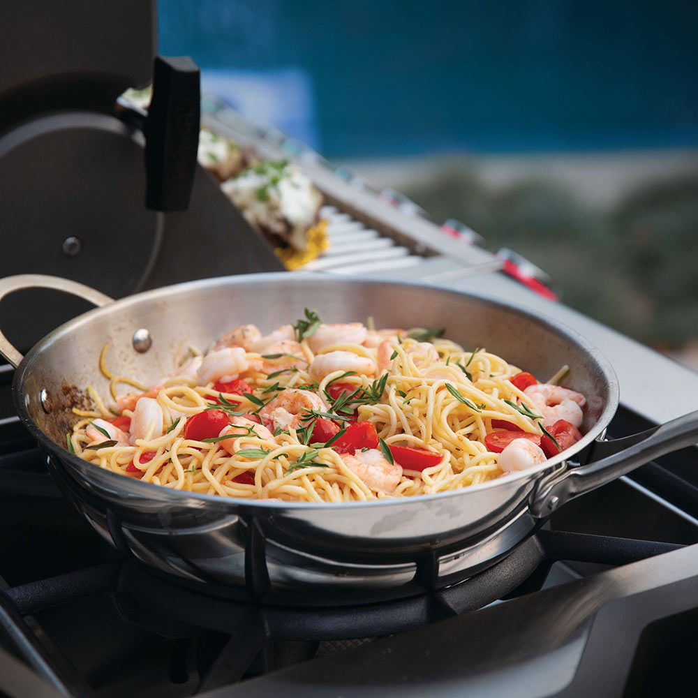 Gas grill cooking surface with a skillet of noodles and vegetables