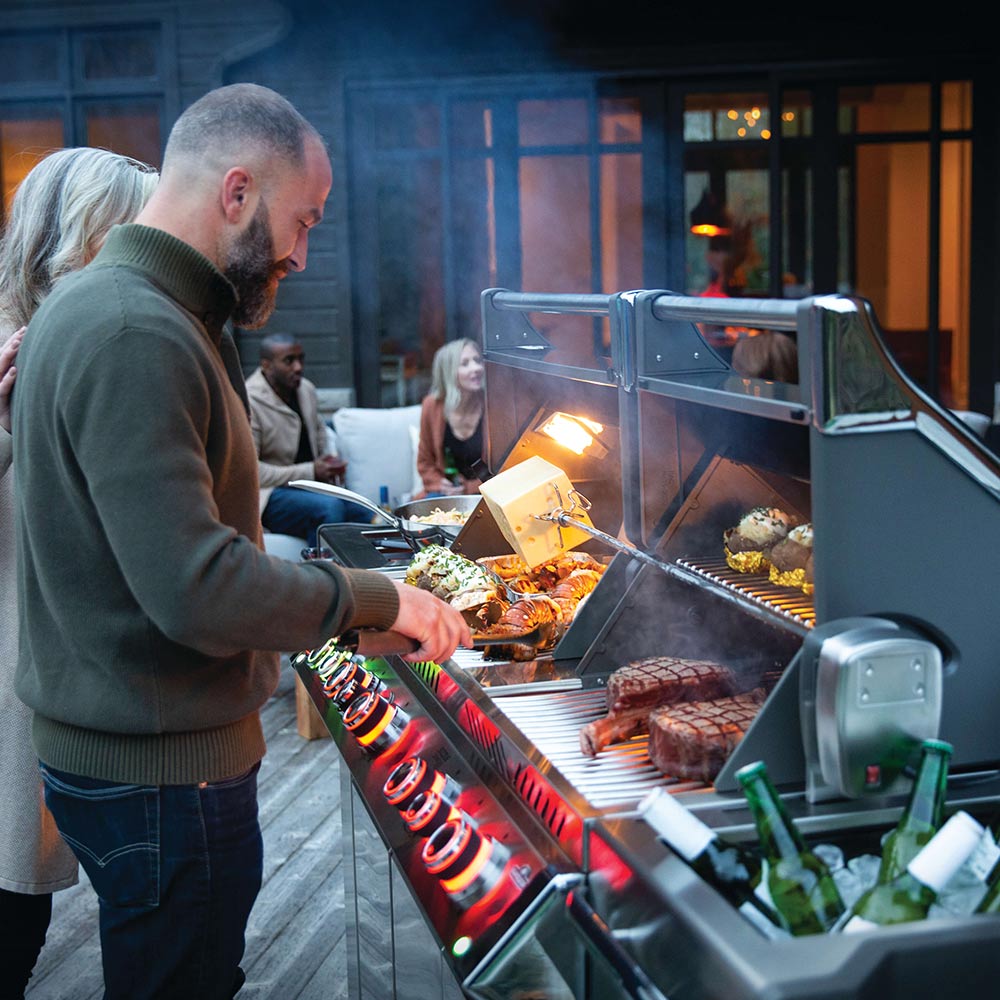 Gas grill with hood open and food cooking on the main burners