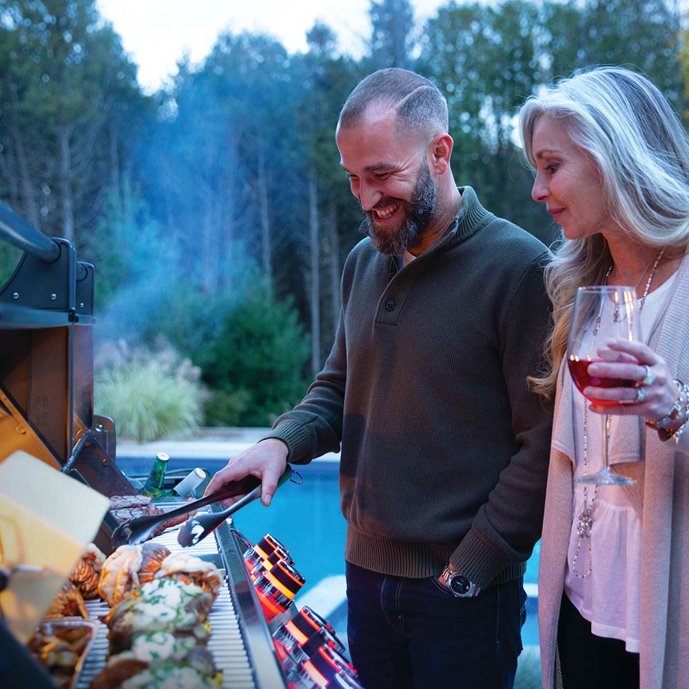 Gas grill cart with food on the cooking grates and smoke rising