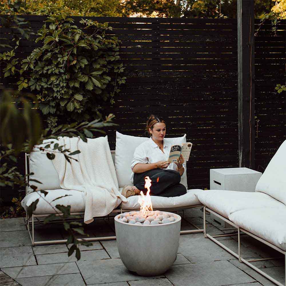 Concrete propane tank cover supporting a backyard fire bowl with visible flames and stones.