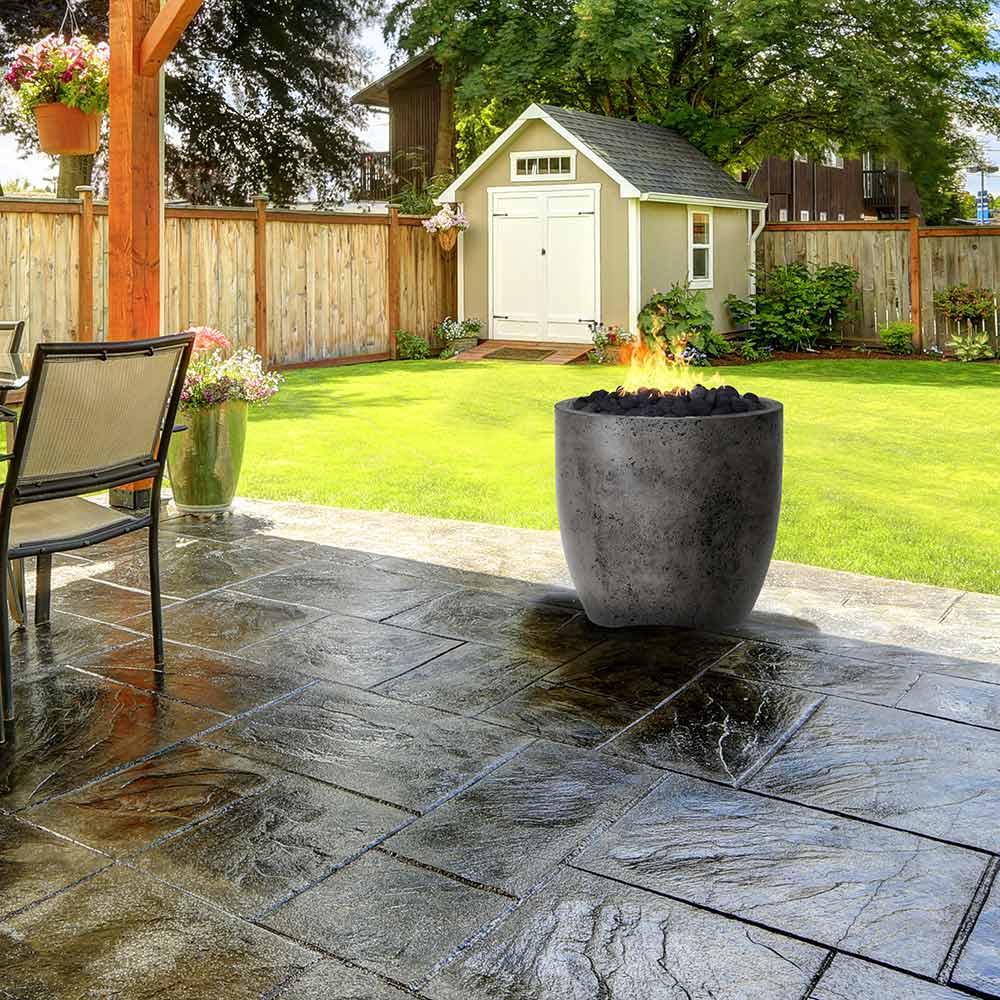 Concrete gas fire pit with dark gray speckled bowl on outdoor stone patio