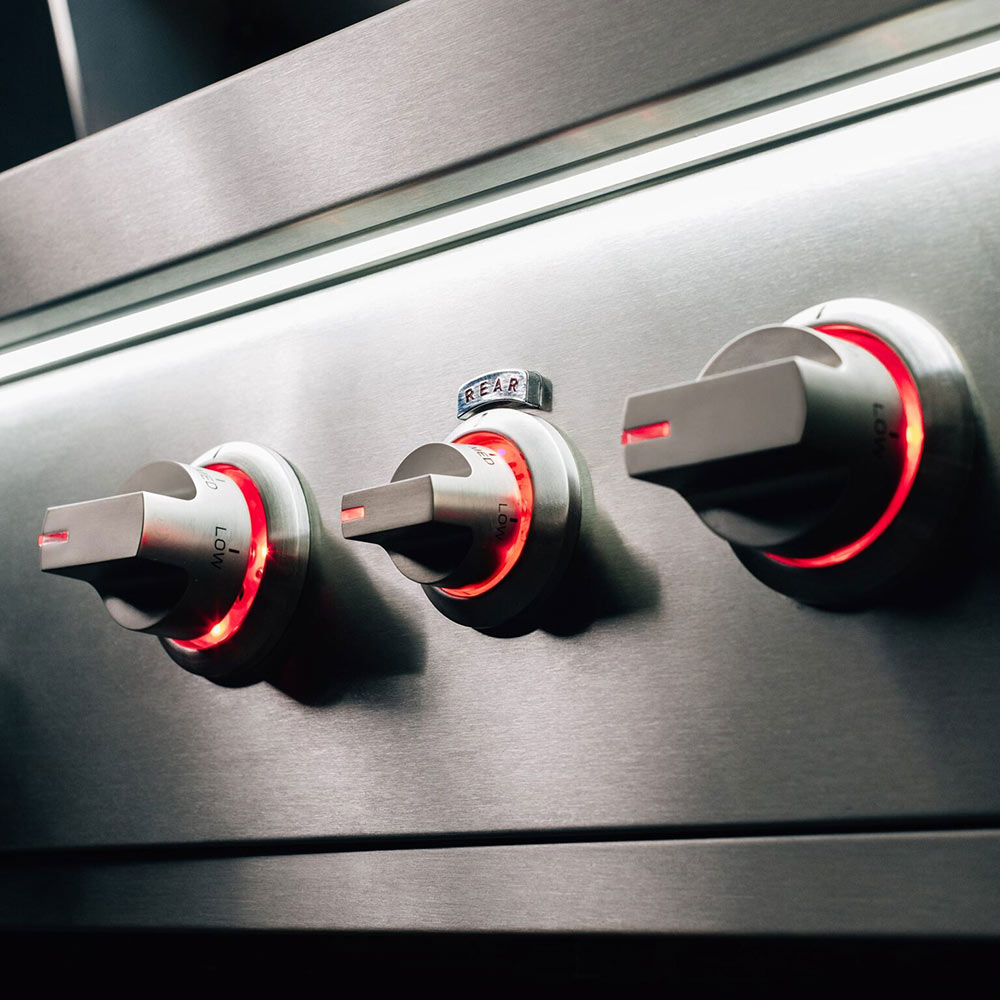 Gas grill control panel with large knobs and red illuminated indicator lights