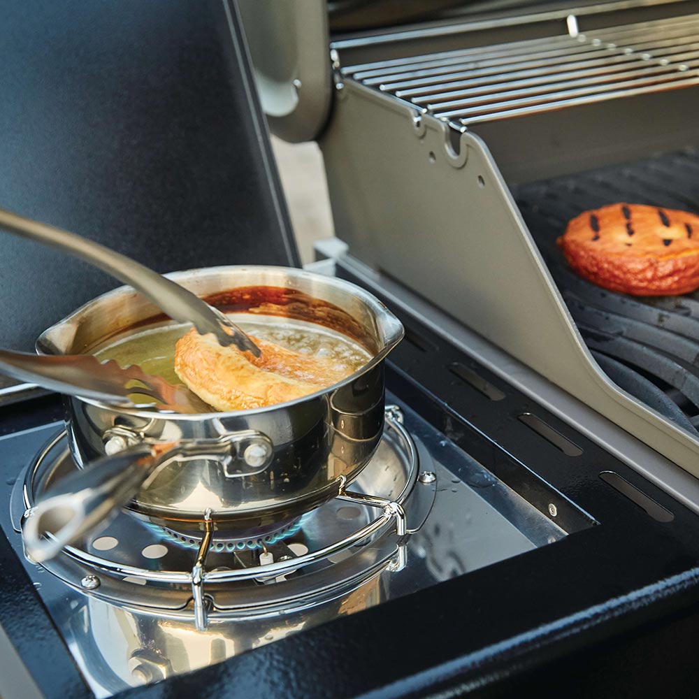 Gas grill cooking grate with a pan on burners and food being cooked