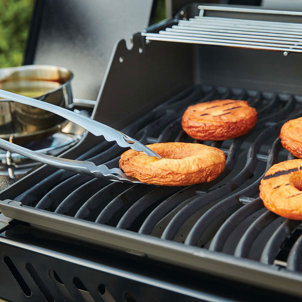 Gas grill grate with sliced vegetables cooking over burners