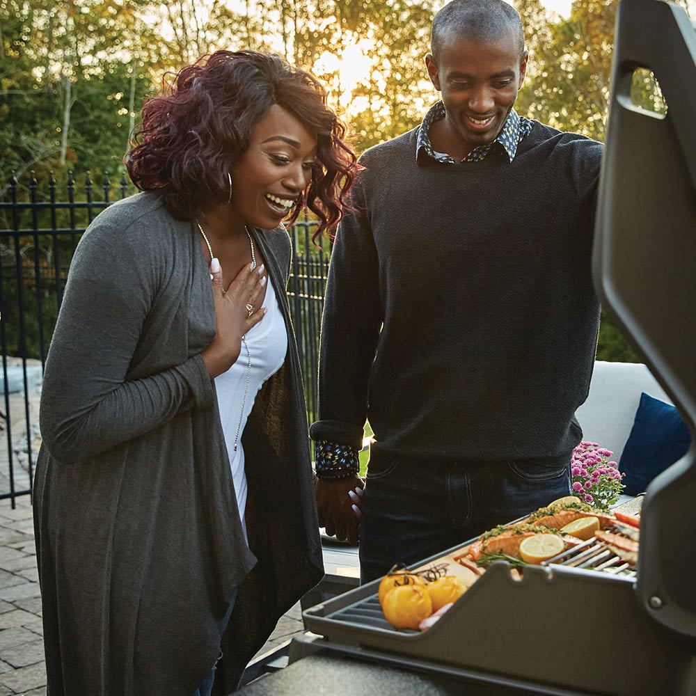 Black gas grill on patio with open lid and cooking surface ready to use