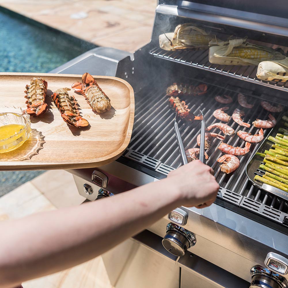Hand grilling with tongs on an infrared grill, with shrimp and asparagus cooking