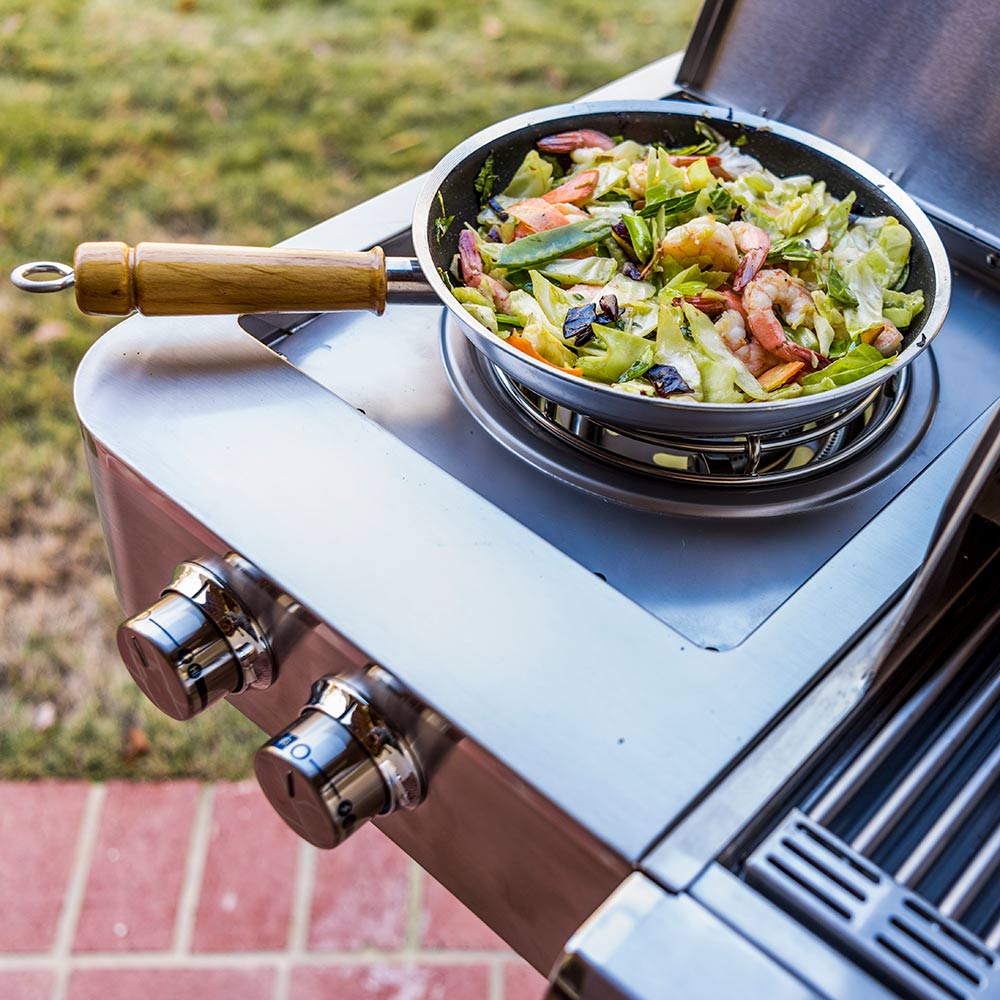 Skillet with salad on the side burner of a stainless steel infrared grill