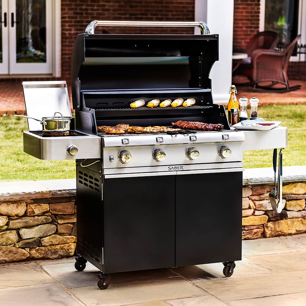 Black infrared grill with lid open and grilled burgers on warming grate, side burner with pan
