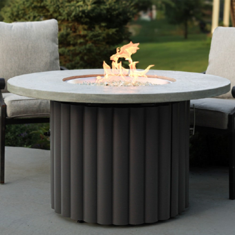 Round gas fire pit table with glowing flames, light gray top, dark ribbed base