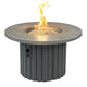 Round gas fire pit table with gray stone top and dark fluted base; fire bowl with flames.