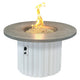 Round gas fire pit table with gray stone top and white fluted base; flames in center bowl.