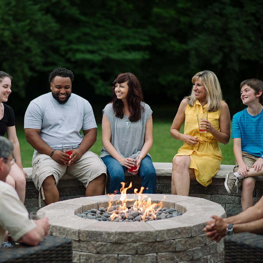Outdoor gas fire pit with flames burning in a round stone fire bowl