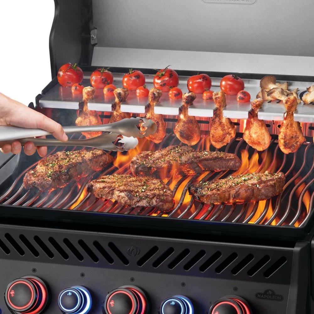 Gas grill grates with skewers and steaks cooking with visible flames