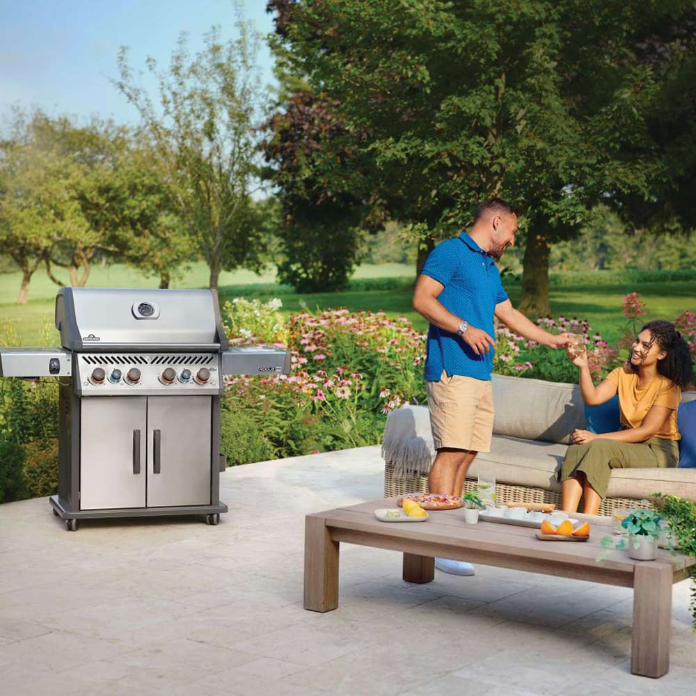 Stainless steel gas grill on an outdoor patio with control knobs and double doors