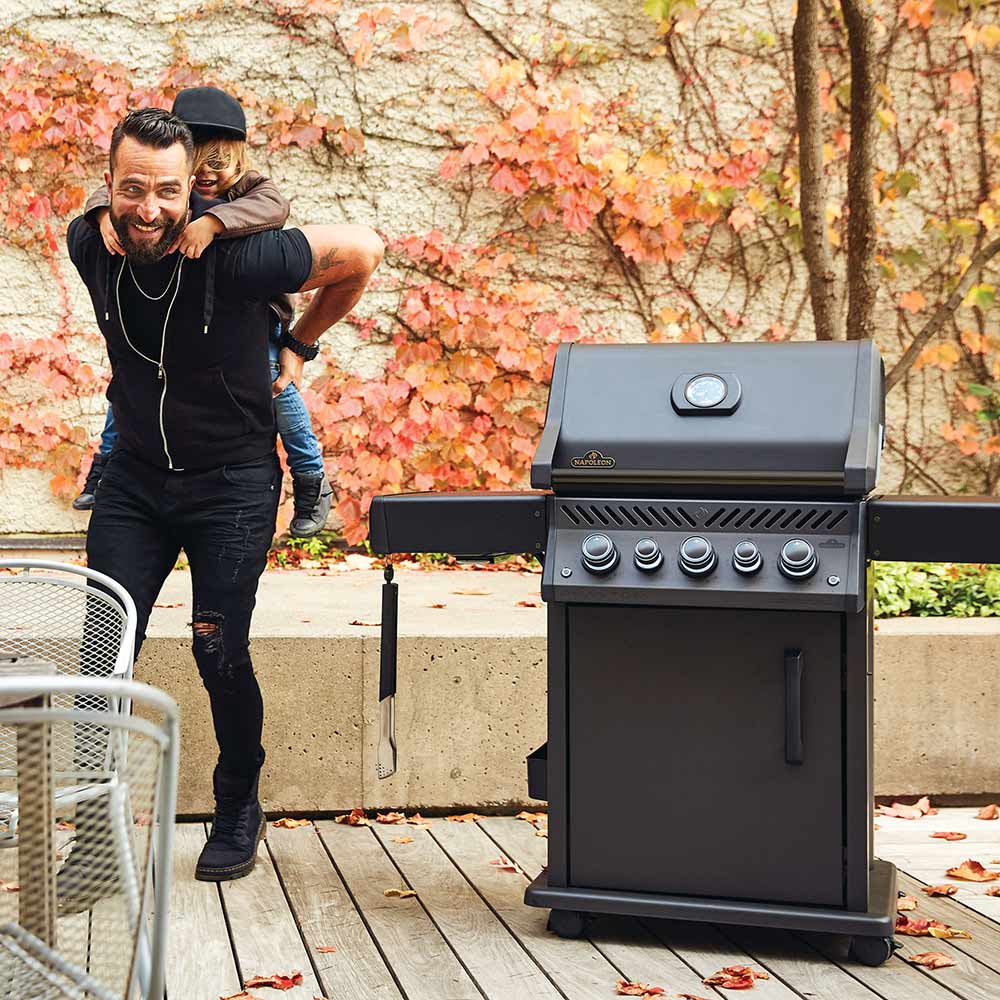 Black gas grill on cart outdoors with man standing beside it