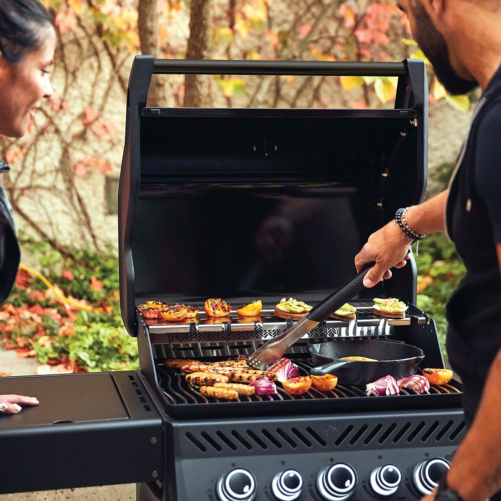 Black gas grill lid open with food cooking on grates